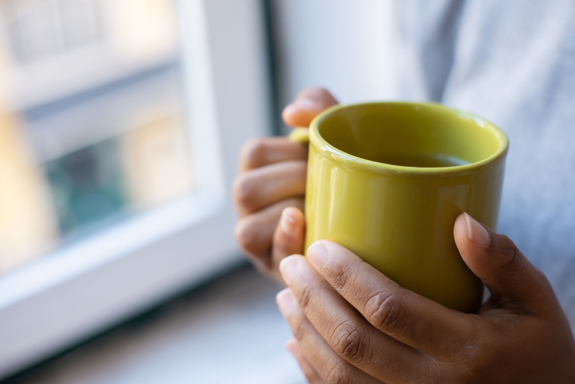 Mains tenant une tasse de café près d'une fenêtre le matin