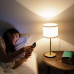 Bruit blanc, rose ou brun : lequel pour dormir ? Personne au lit consultant son smartphone le soir pres d une lampe
