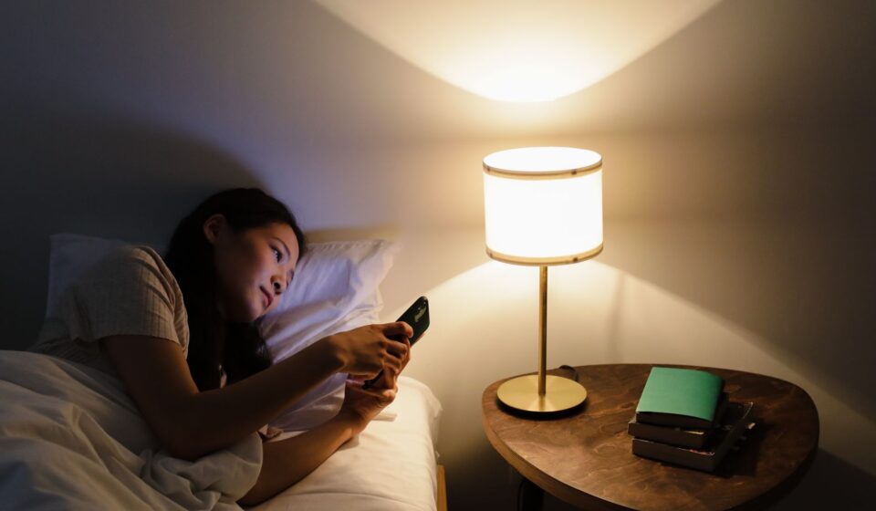 Personne au lit consultant son smartphone le soir pres d une lampe