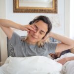 Dette de sommeil : peut-on vraiment la rattraper ? Jeune femme qui s etire au reveil dans son lit le matin