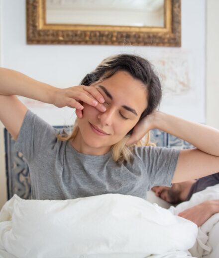 Dette de sommeil : peut-on vraiment la rattraper ? Jeune femme qui s etire au reveil dans son lit le matin